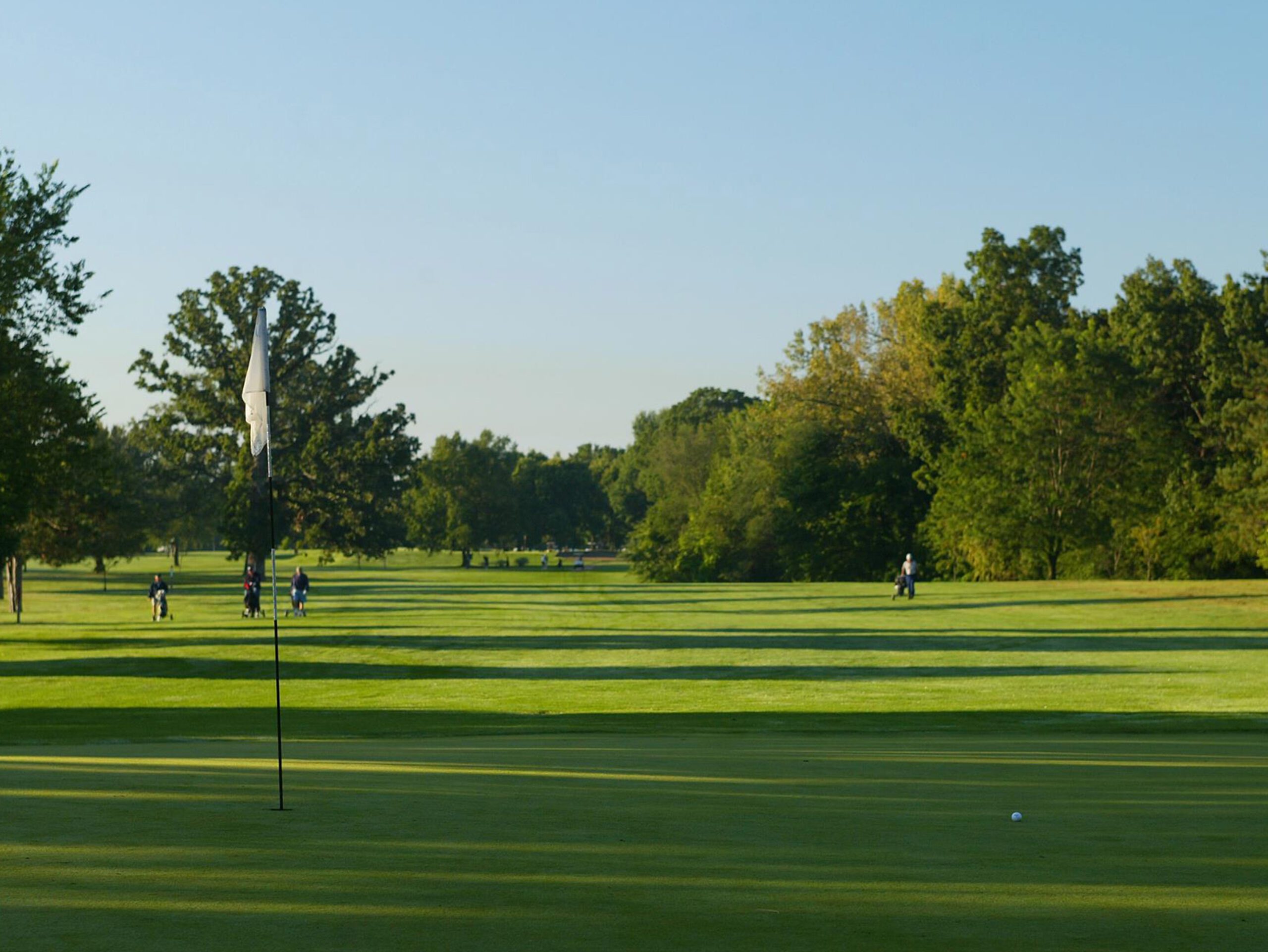 Golf course with players and trees.