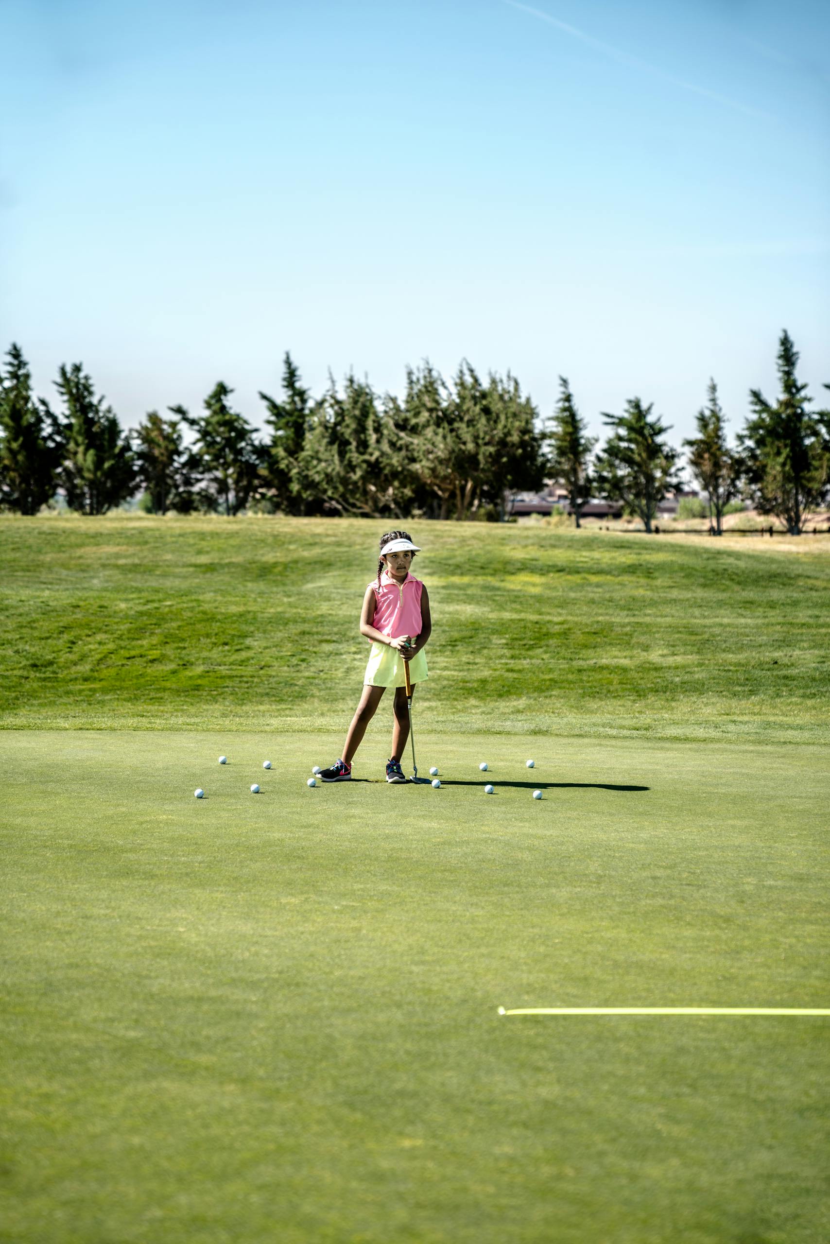 A young girl practicing her putting skills on a sunny golf course.